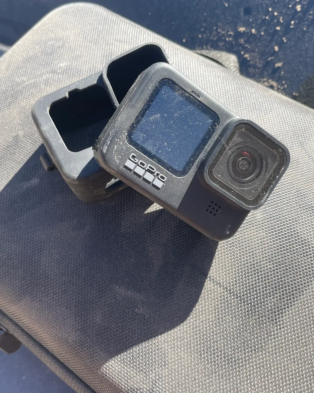 A dusty action camera resting on its padded case in bright sun